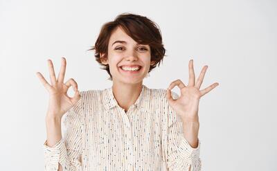 Portrait of natural happy woman with short hairstyle, showing okay gestures and smiling, approve and like something, show positive feedback, white wall