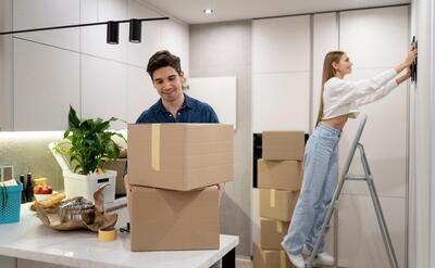 Woman hanging frame on the wall while her boyfriend is handling boxes