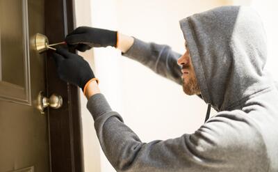 Man with a hoodie trying to pick a lock in a house.