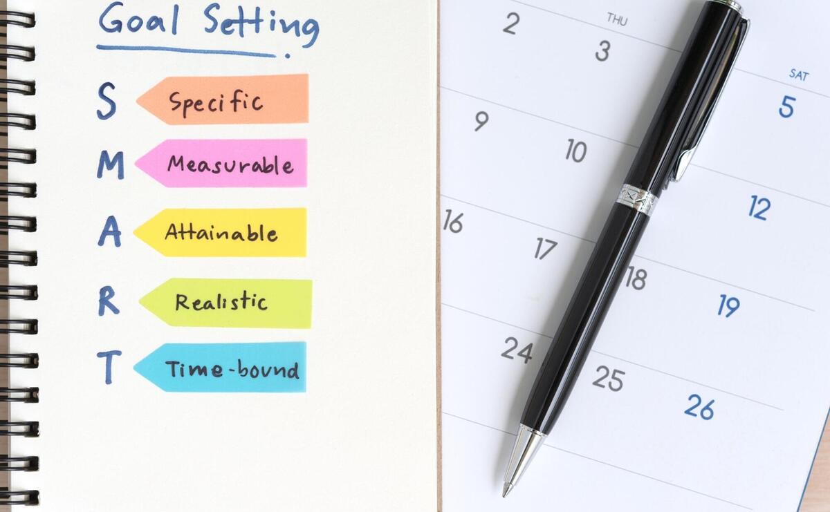 Notepad with SMART goal attributes listed beside a pen and calendar.