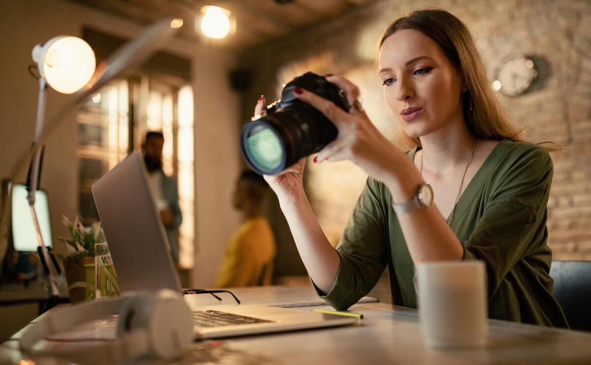 Low angle view of female photographer looking at photos on camera while working late in the office