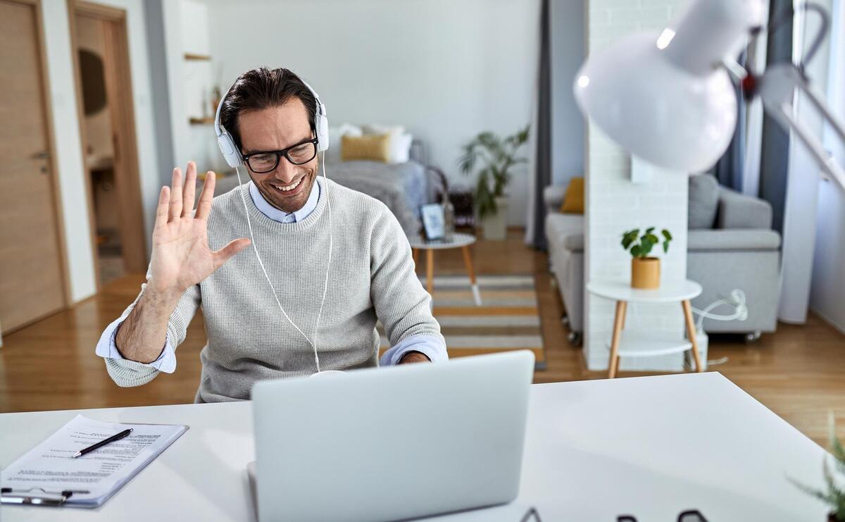 Man waving while having online meeting over laptop from home.