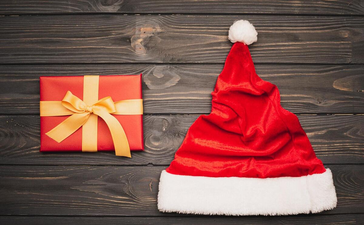 Red gift box and Santa hat on rustic wooden background.