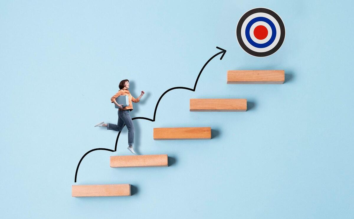 Woman ascending steps towards a target on a blue background.